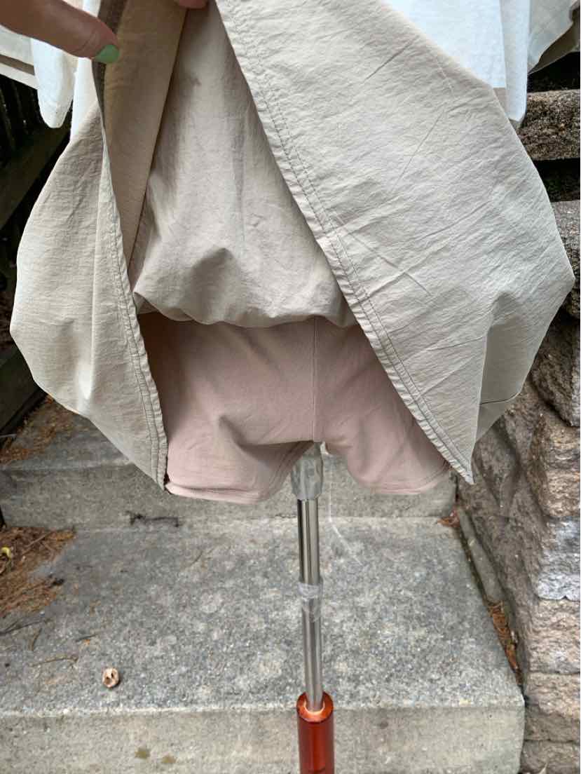 Tan textured fabric with draped layering over light tan fitted shorts on a stand.