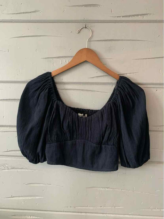 Black cropped blouse with puffed sleeves and gathered neckline on a wooden hanger against white wall.