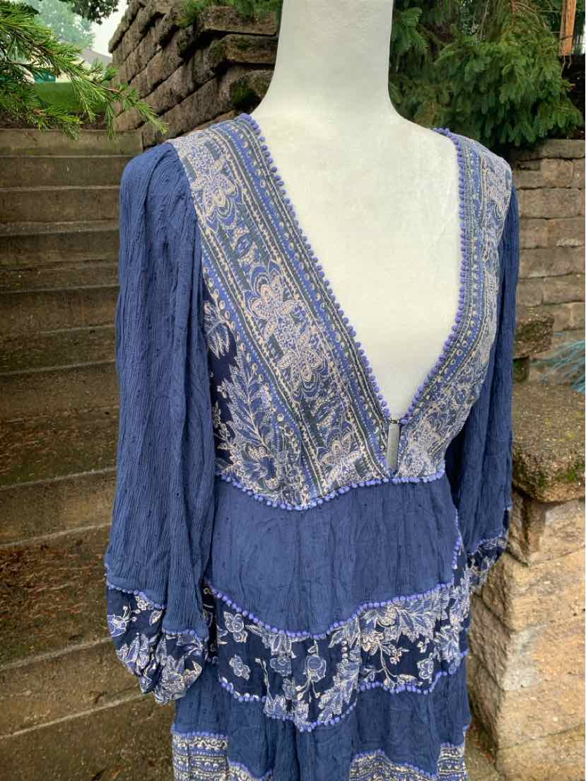 Blue long-sleeve dress with deep V-neck, intricate white floral embroidery, and tiered skirt layers.
