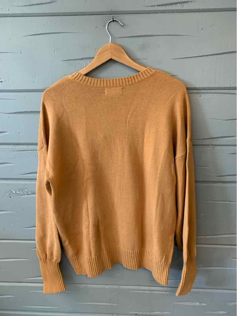 Camel-colored knit sweater with ribbed cuffs and hem hanging on wooden hanger against gray paneled wall.