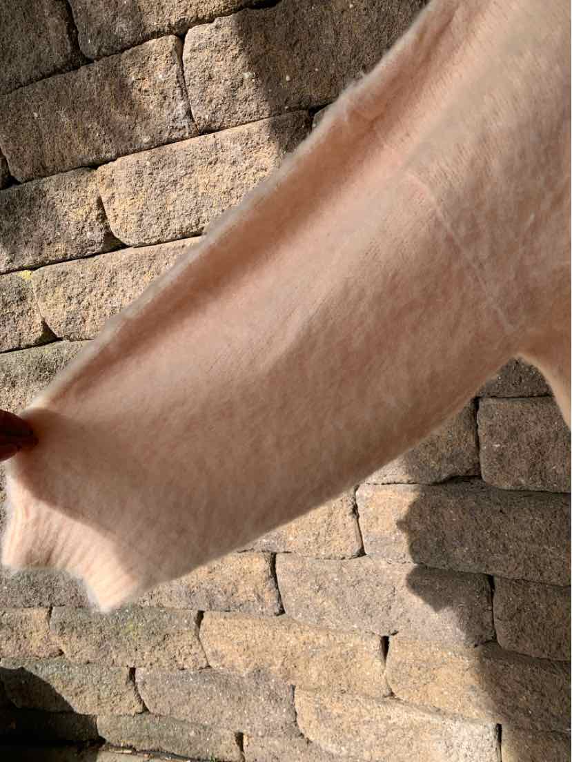Close-up of a soft, solid peach fabric garment with a fuzzy texture and hem against a stone wall.