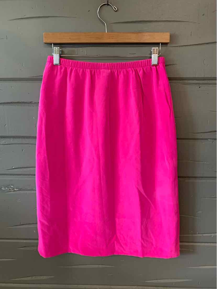 Bright pink knee-length skirt with elastic waistband hanging on wooden hanger against gray wooden wall.