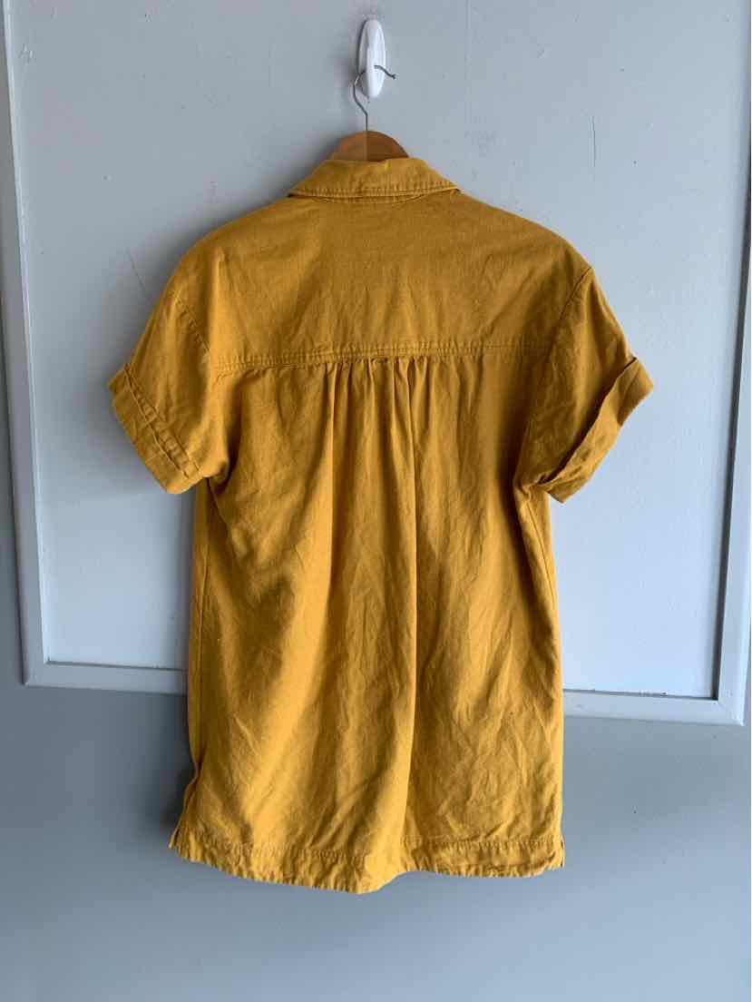 Mustard yellow short-sleeve blouse with button-up front and relaxed fit hanging on wooden hanger.