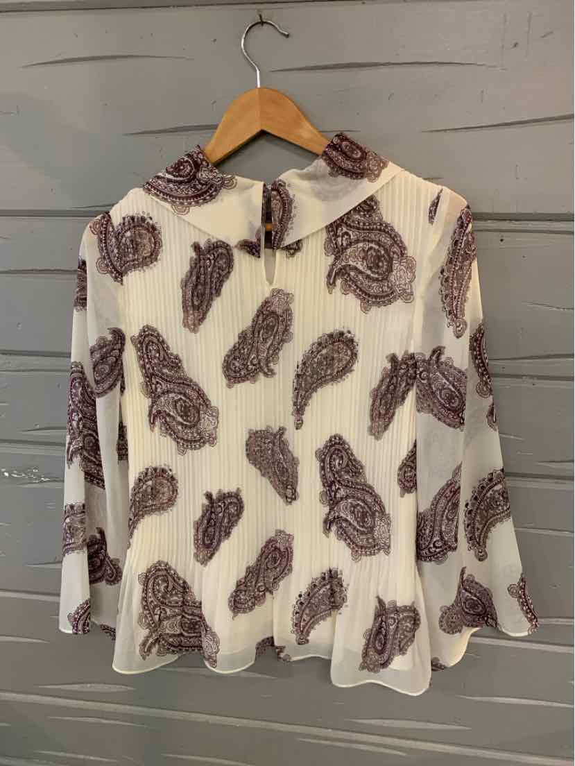 White blouse with brown paisley print, long sleeves, and button-up front on wooden hanger.