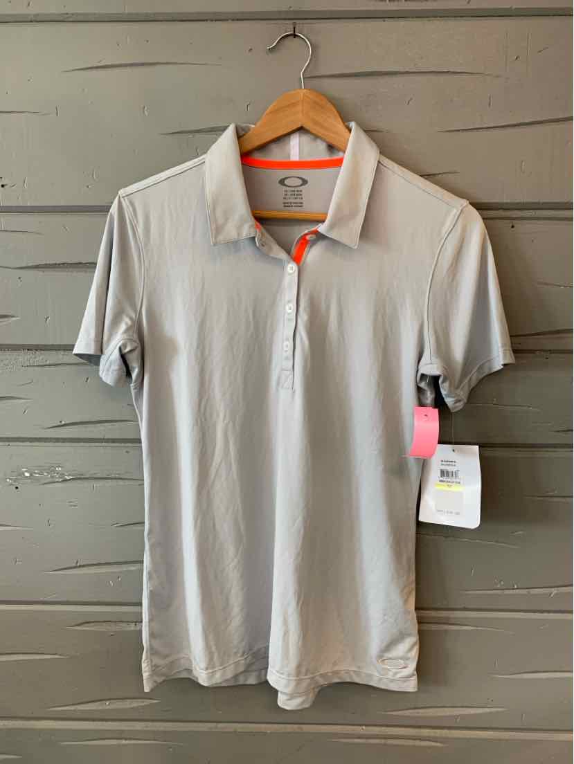 Light gray oakley polo shirt with short sleeves and a three-button placket on a wooden hanger.