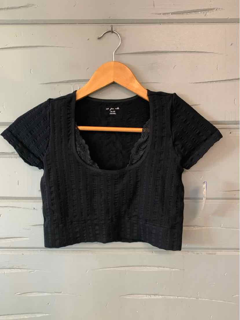 Black cropped short-sleeve top with a scoop neckline and textured fabric, hanging on a wooden hanger.