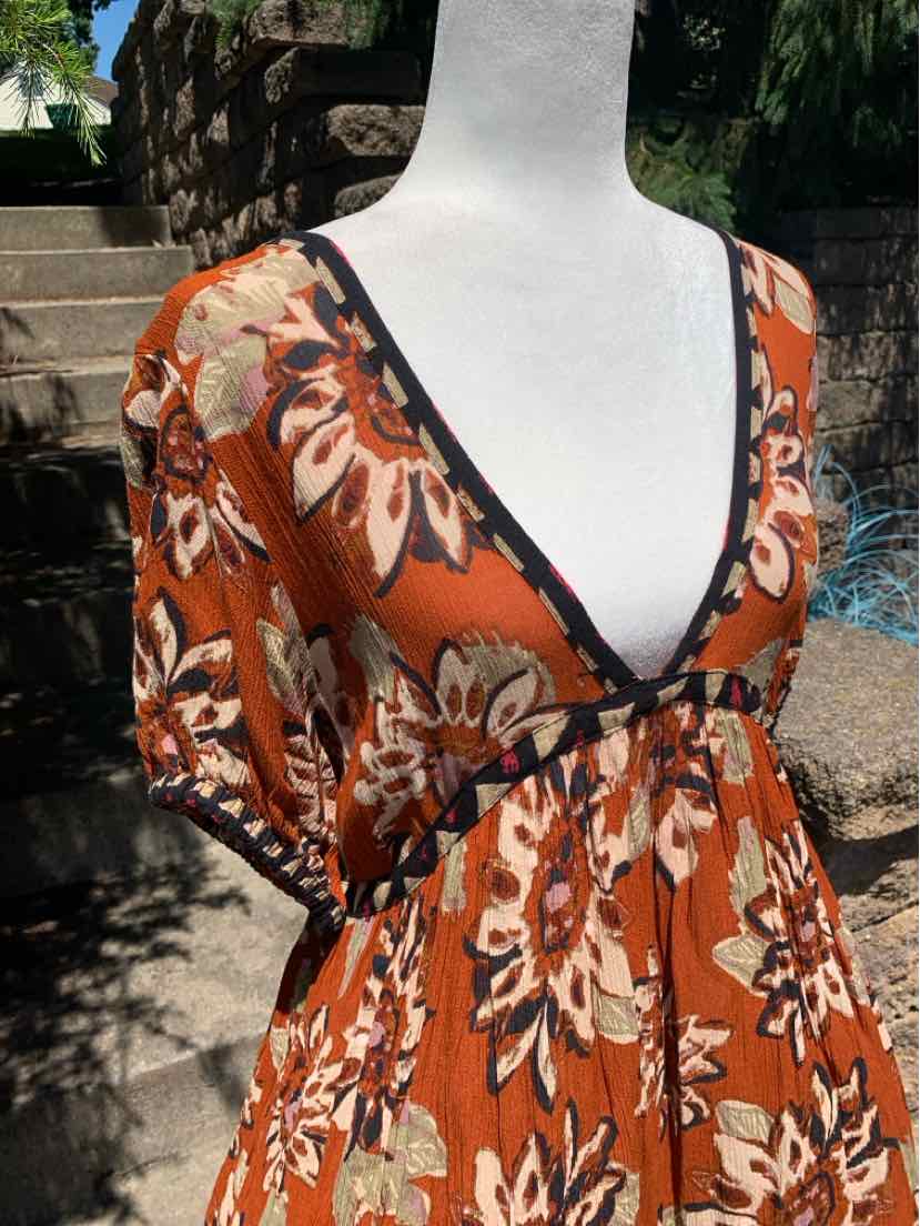 Rust-orange patterned midi dress with deep V-neckline, black trim, and short puff sleeves.