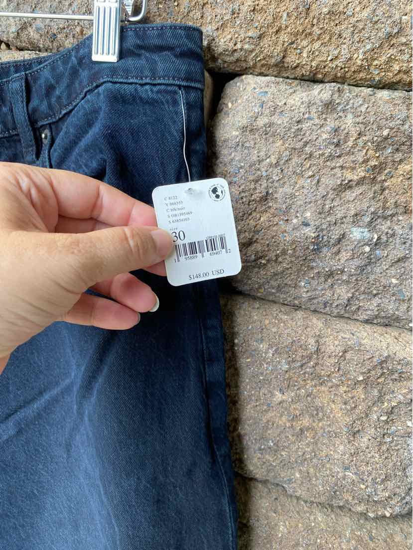 Hand holding white size 10 tag attached to black denim pants against a stone wall background.