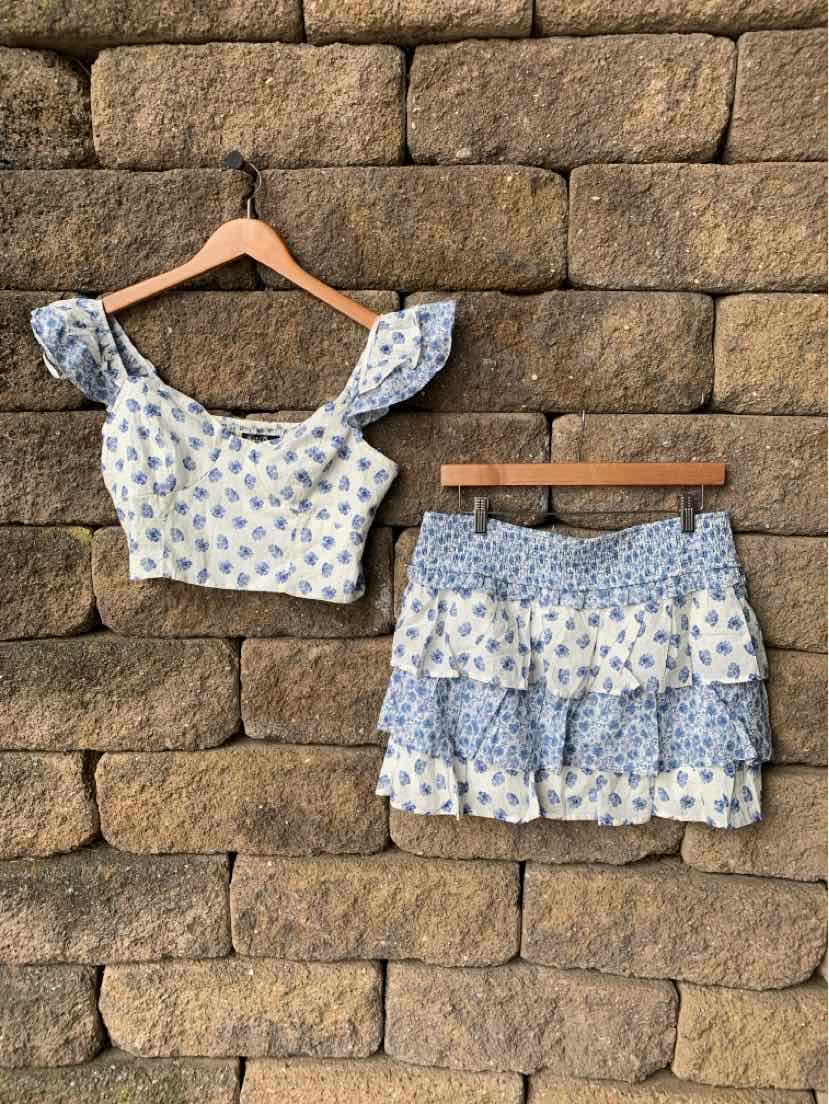 Blue paisley print two-piece outfit with ruffled crop top and tiered mini skirt on wooden hangers.