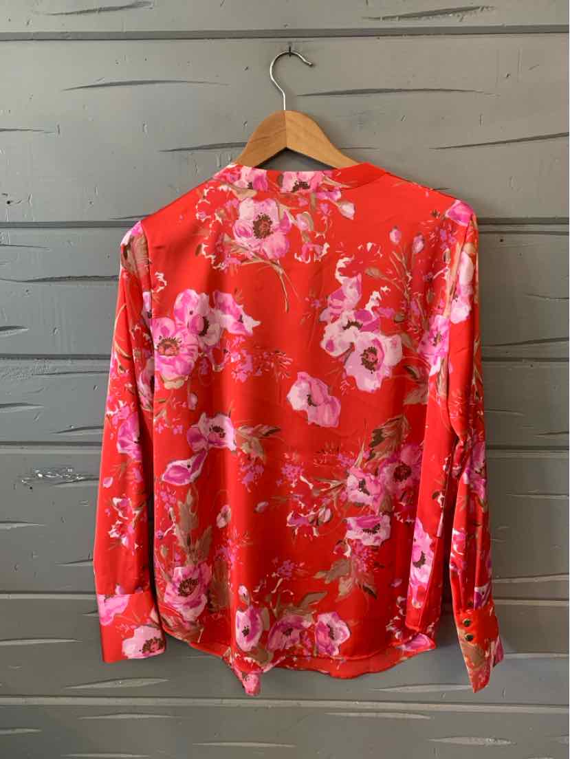 Coral pink long-sleeve blouse with bright floral print and buttoned cuffs on wooden hanger.