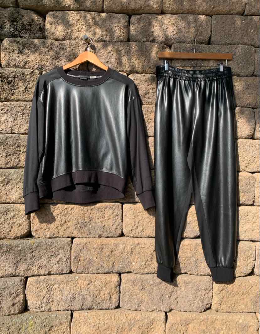 Black two-piece set with a relaxed long-sleeve top and tapered jogger pants in a glossy leather-like finish.