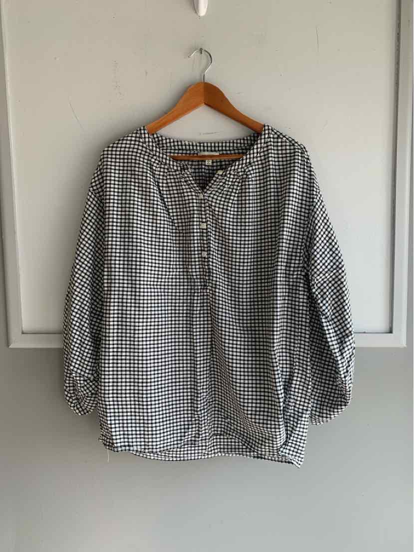 Black and white gingham checkered long sleeve blouse with buttoned neckline on wooden hanger.