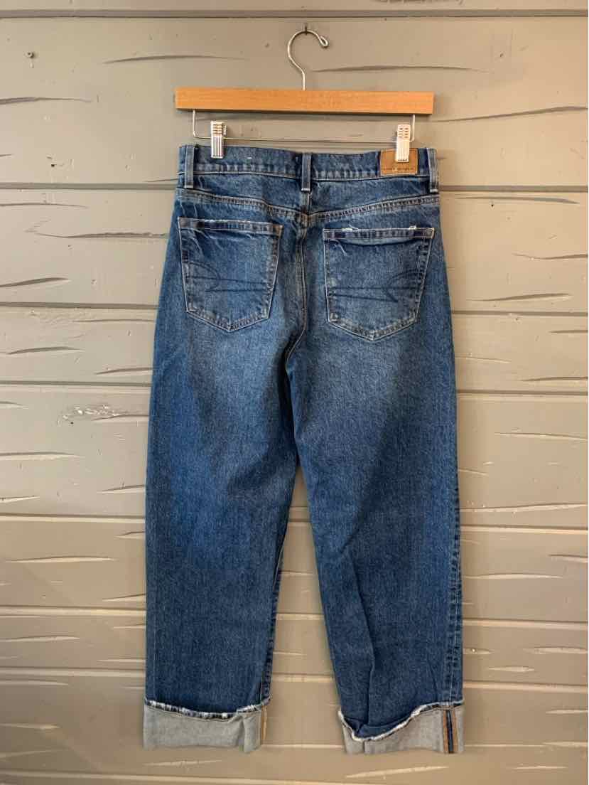 Blue denim American Eagle jeans size 2 with folded cuffs and back pockets, hanging on wooden hanger.