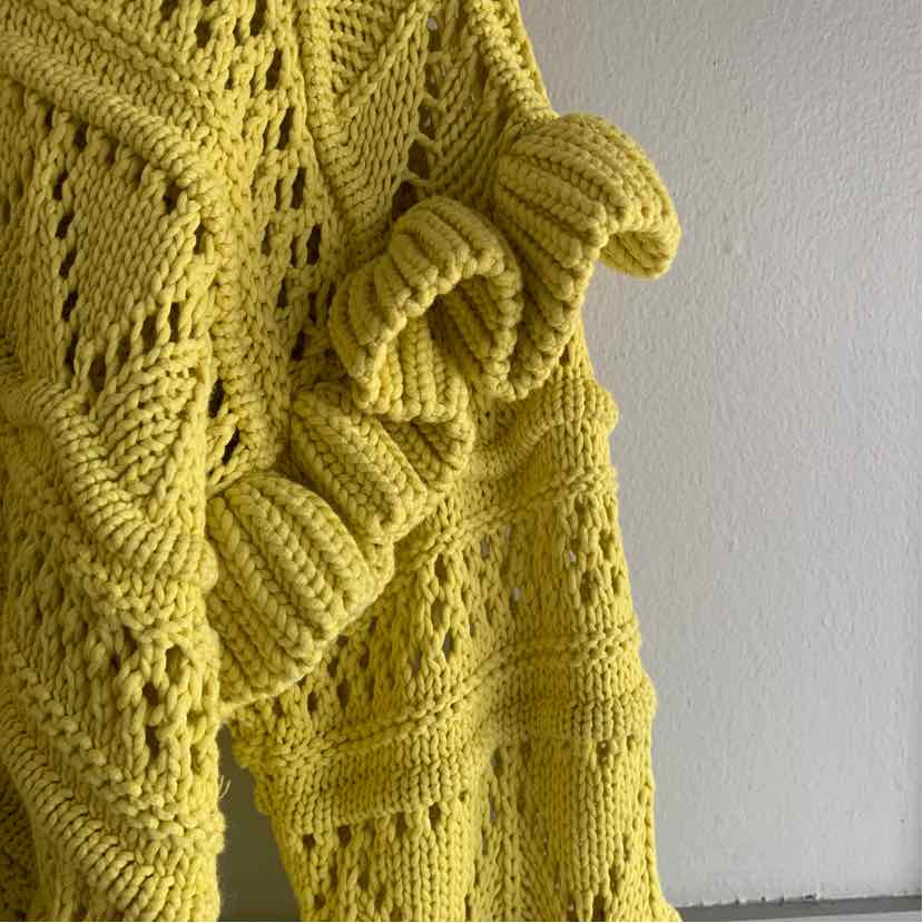 Yellow knitted sweater with textured patterns and ruffled details on sleeves.