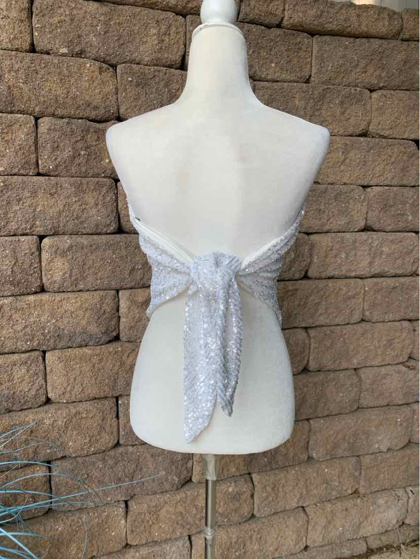 Silver sequin tie-back bandeau crop top with strapless design on mannequin against stone wall background.