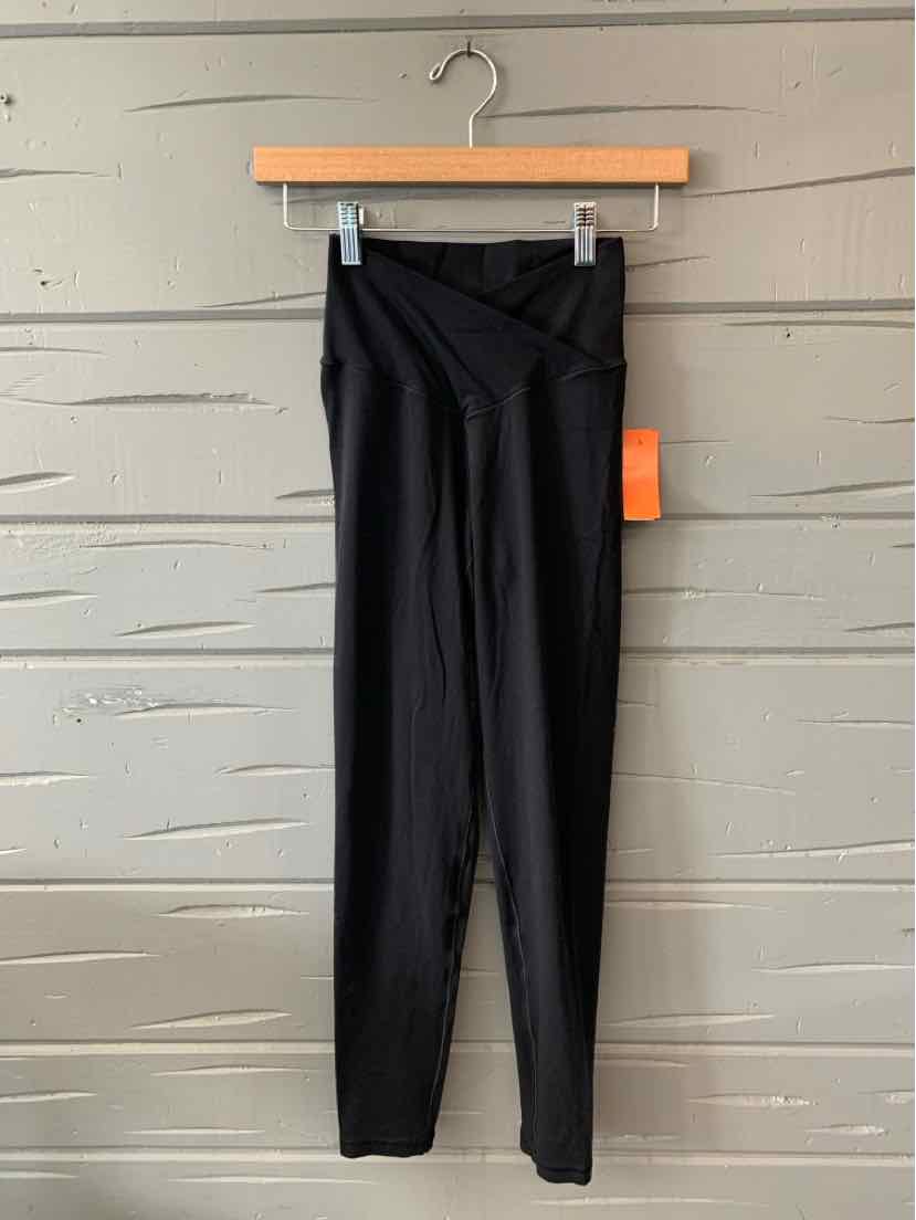 Black high-waisted leggings with a wide waistband and a tight, stretchy fit hanging on a wooden hanger against a gray.