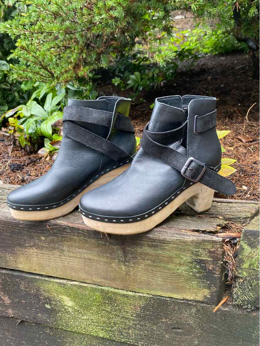 Black leather ankle boots with wooden platform heels and decorative side buckle straps.