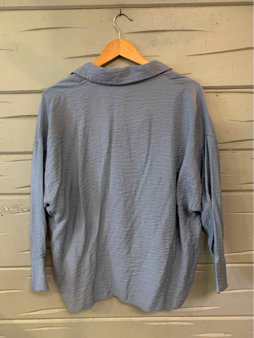 Light blue long-sleeve blouse with collar, relaxed fit, and textured fabric hanging on wooden hanger.