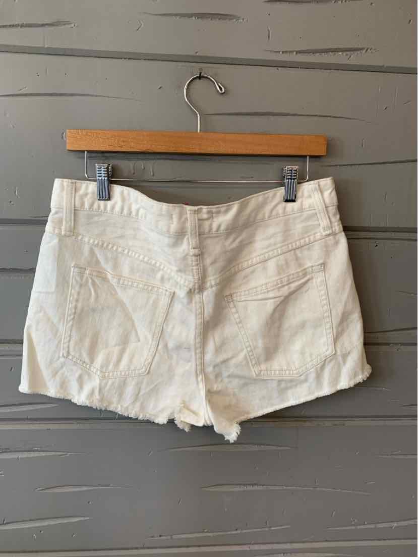 White denim shorts with frayed hems, front and back pockets, and a fitted waistband on a wooden hanger.