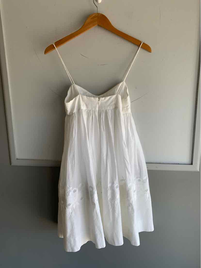 White sleeveless dress with thin straps and gathered bodice on wooden hanger.