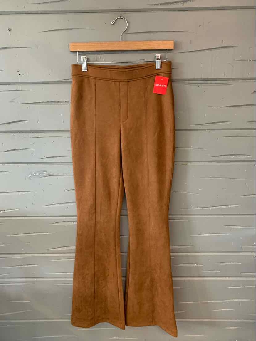 Tan high-waisted stretchy Spanx pants with a flared leg and front seams, size medium, hanging on wooden hanger.
