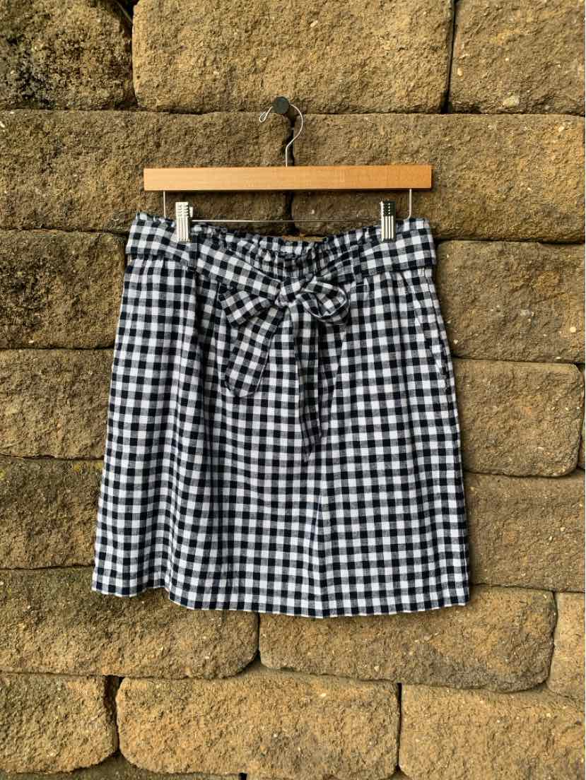Black and white gingham skirt with a tied waist bow, medium size, hanging on wooden hanger.