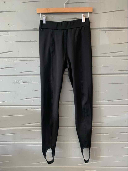 Black high-waist leggings with ankle stirrups hanging on wooden hanger against gray shiplap wall.