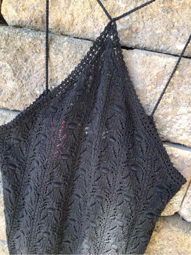 Black medium crochet knit tank top with thin straps hanging on a wire grid background.