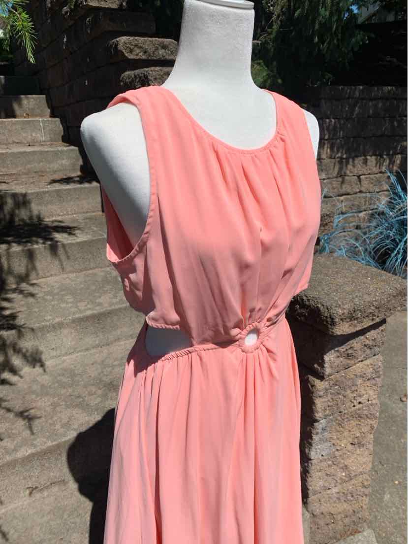 Sleeveless coral pink dress with gathered bodice and decorative buttoned waist cutout on mannequin.