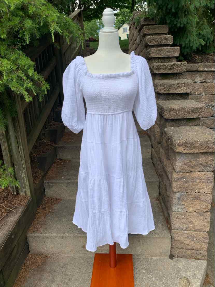 White midi dress with puffed elbow-length sleeves and square neckline on a mannequin outdoors.