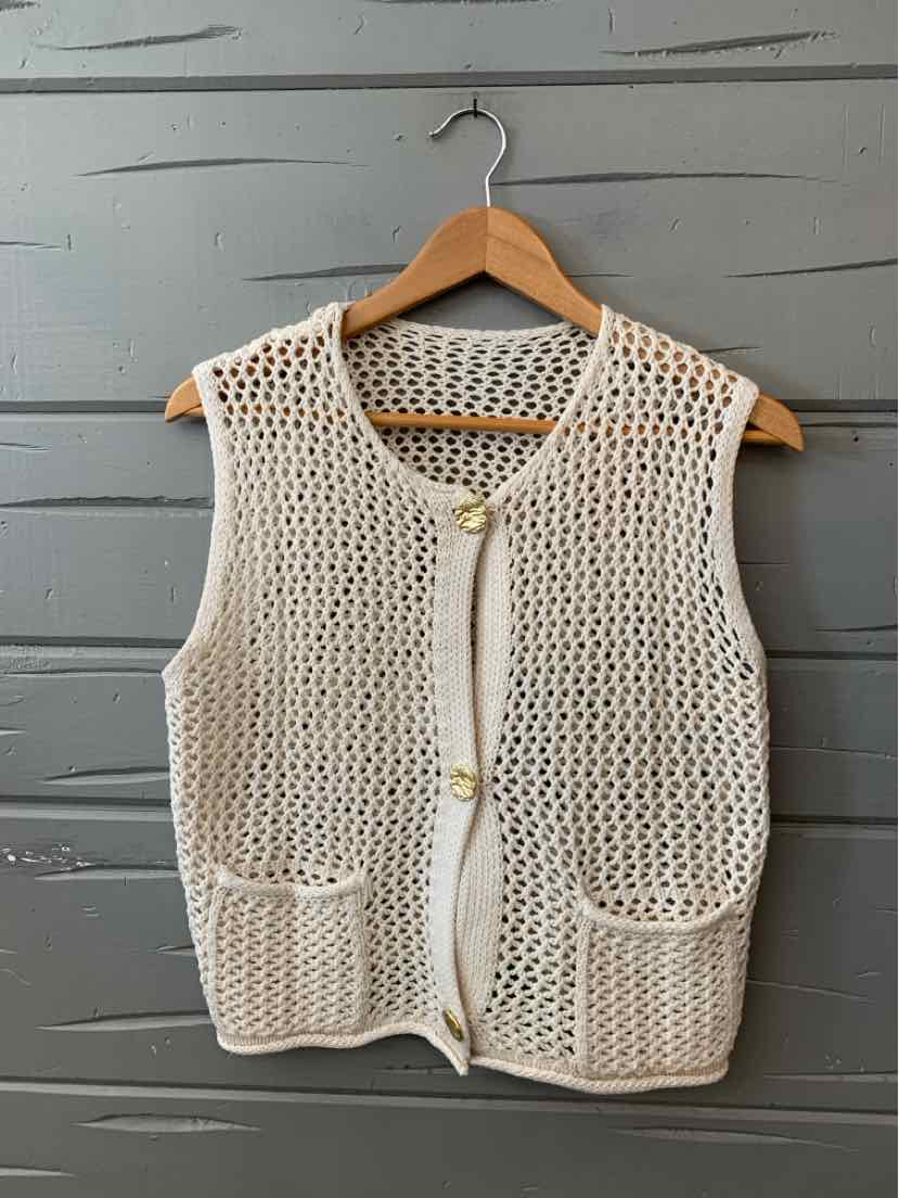 Cream-colored knit sleeveless vest with front pockets and button closure on wooden hanger.