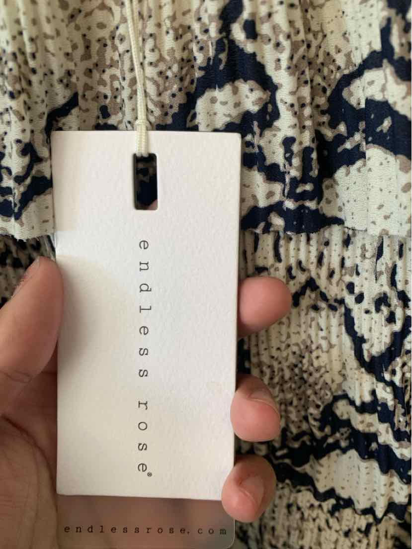 White clothing tag with black Endless Rose logo and med size text held against a black and beige lizard pattern fabric.