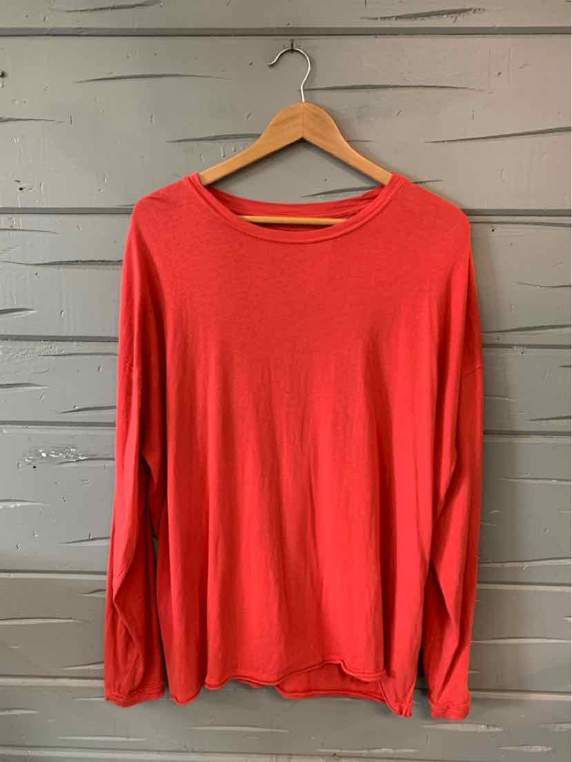 Long-sleeve red crewneck shirt with a relaxed fit hanging on wooden hanger against gray wooden wall.