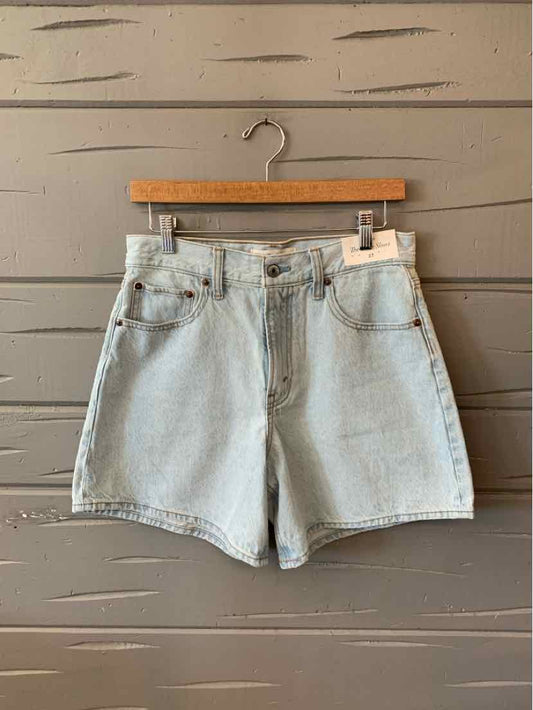 Light blue high-waisted denim shorts with front pockets and belt loops on wooden hanger.