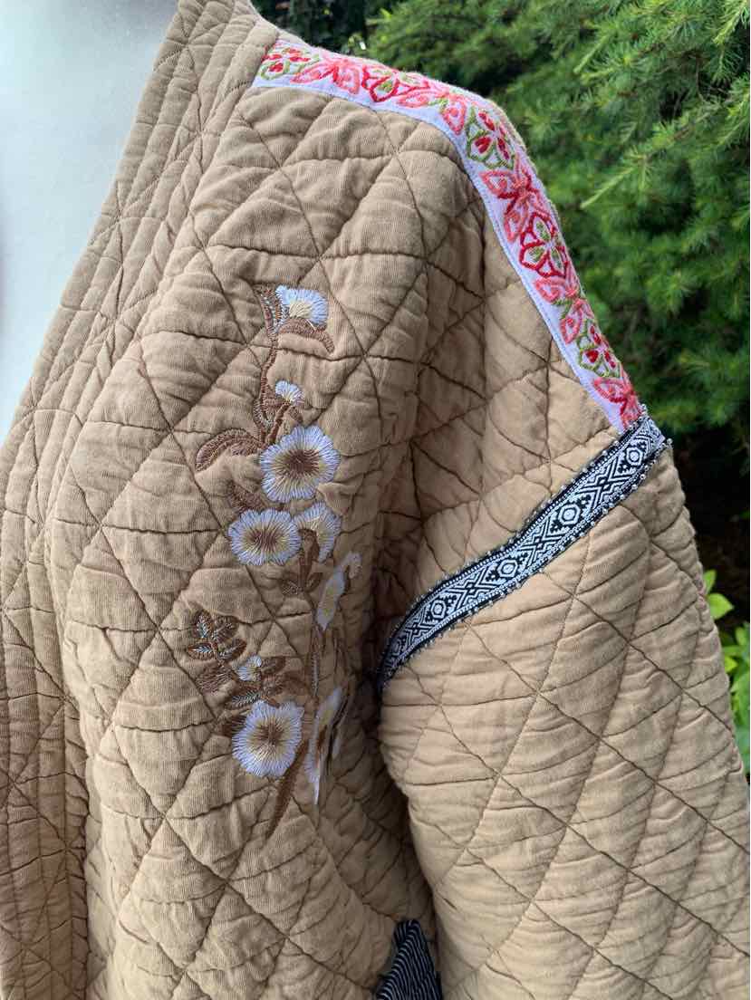 Tan quilted jacket with diamond stitching, floral embroidery on sleeve, and pink patterned trim along shoulder.