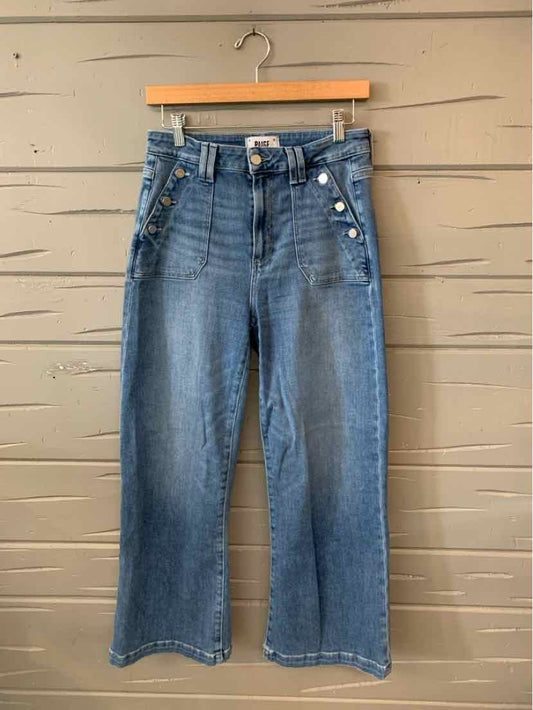 High-waisted blue denim jeans with wide legs, front button fly, and front patch pockets hanging on wooden hanger.