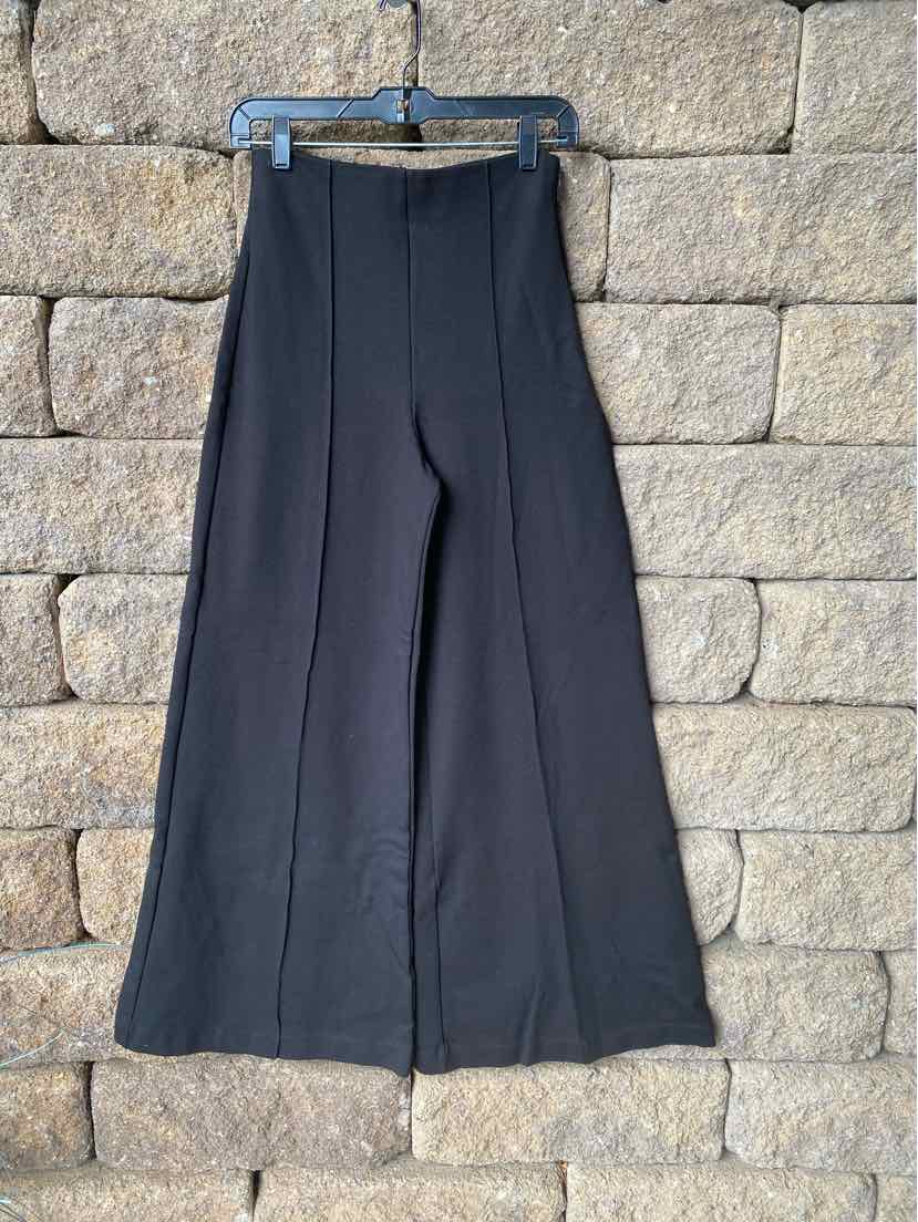 Black high-waist wide-leg pants in medium size with clean seams, hanging against a stone wall background.