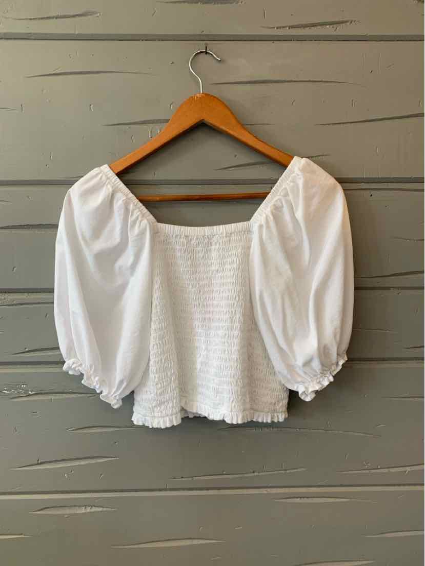 Beige cropped blouse with smocked bodice and puffed three-quarter sleeves on wooden hanger.