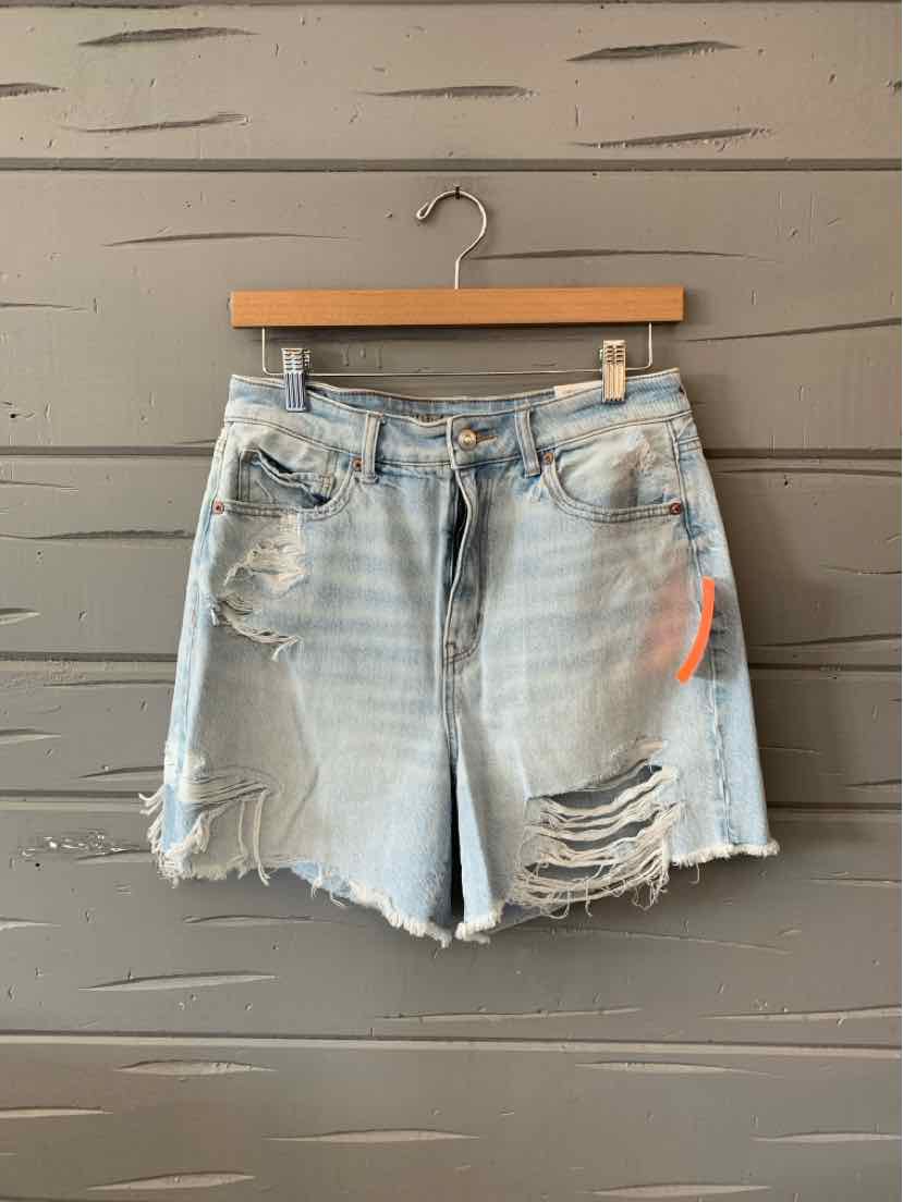 Light blue distressed denim shorts with frayed hems and ripped details on front pockets and thighs, hung on wooden hanger.