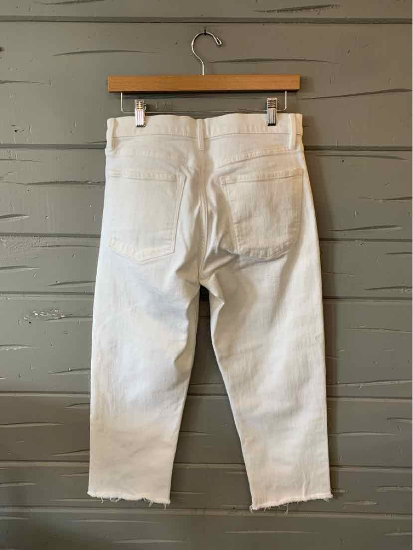 White denim jeans with a straight fit, cropped length, raw hem, and two back pockets hanging on a wooden hanger.