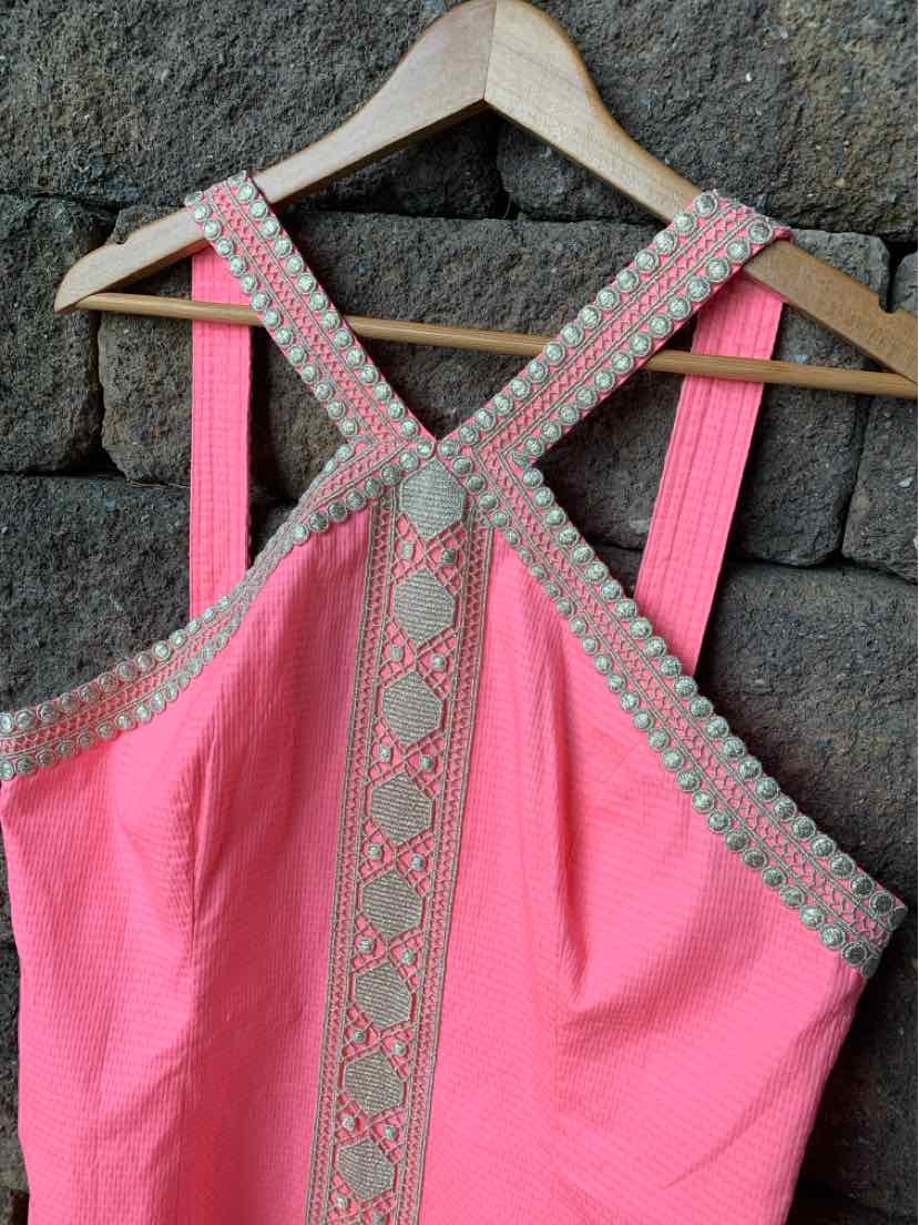 Pink sleeveless dress with cross-back straps and decorative beige embroidery trim.