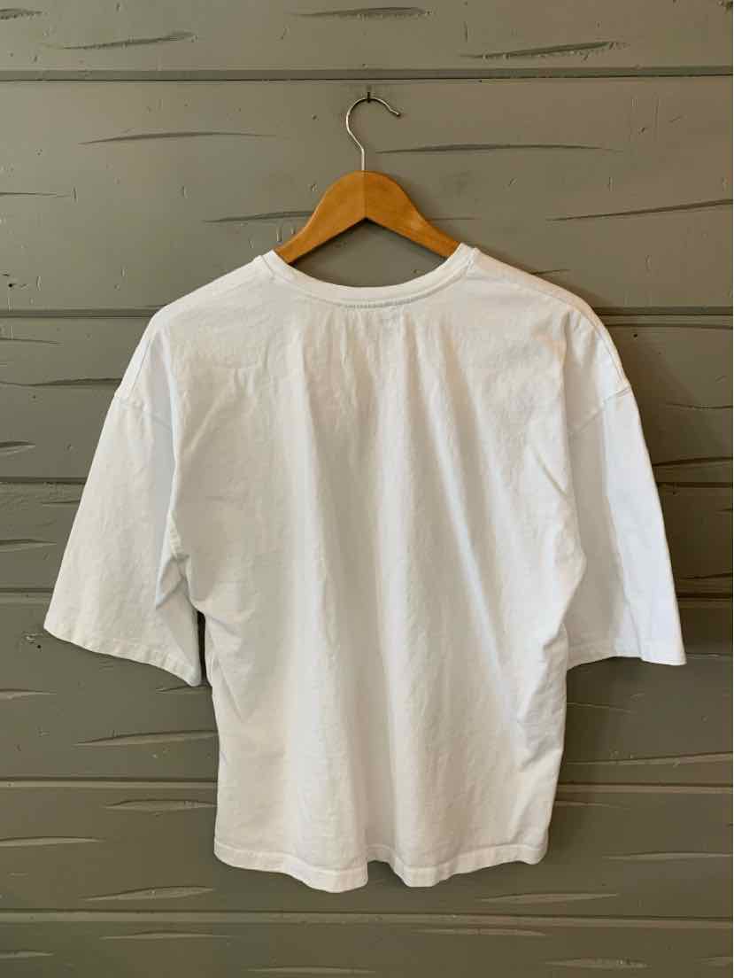 White short-sleeve crew neck T-shirt with relaxed fit on wooden hanger against gray wall.