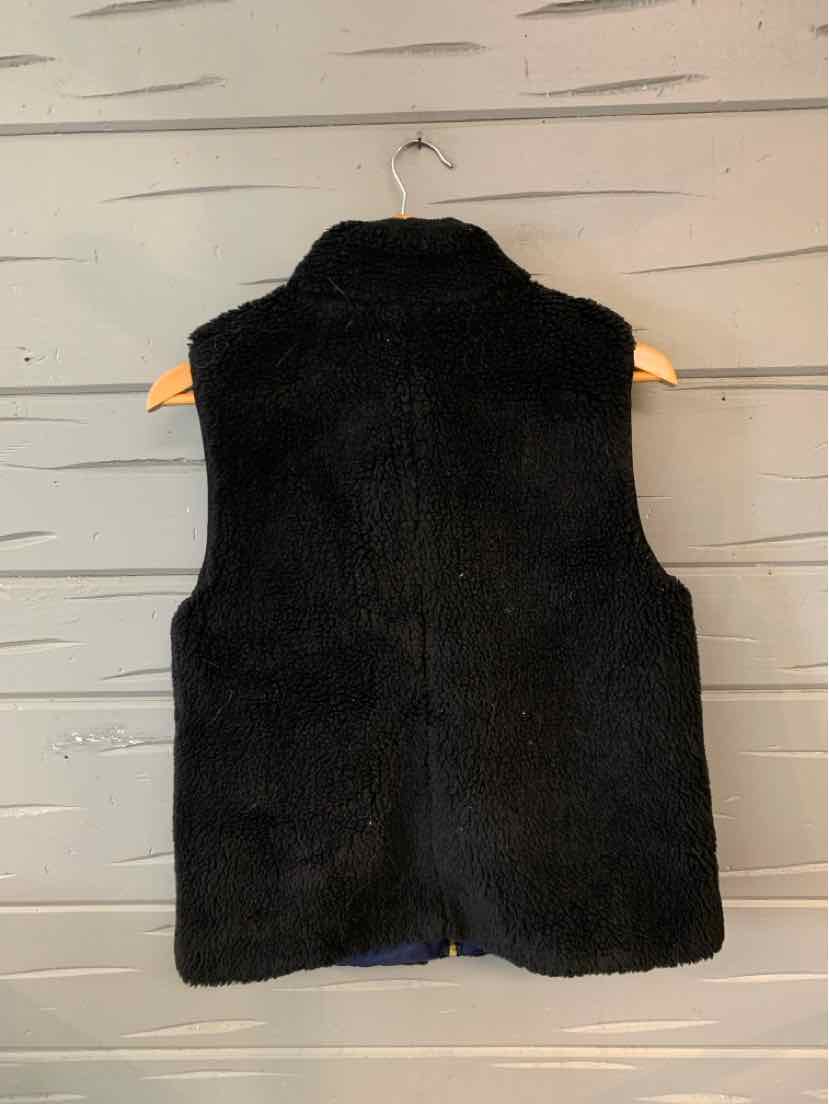 Black sherpa fleece vest with high collar and sleeveless design hanging on wooden hanger.