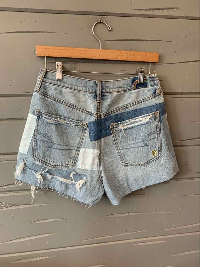 Light wash denim shorts with frayed hems, patchwork details in different shades of blue, and back pockets with button.