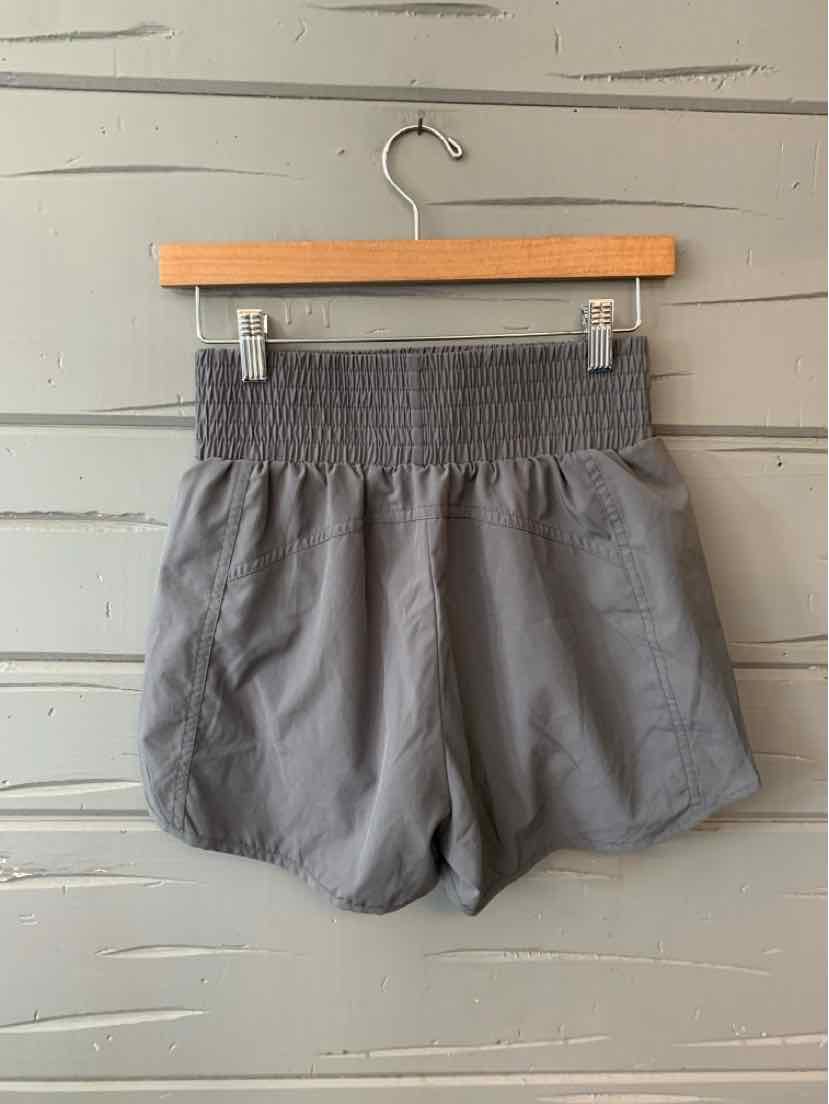 Gray lightweight shorts with wide smocked waistband and relaxed fit hanging on wooden hanger against gray wooden background.