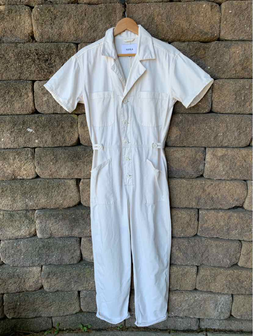 White short-sleeve jumpsuit with lapel collar and front pockets hanging against stone wall.