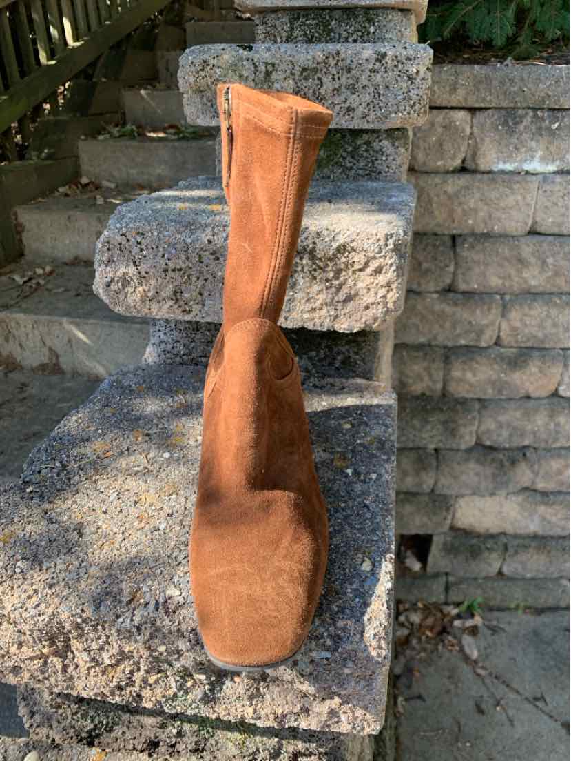 Tan suede knee-high boot with a slim shaft and rounded toe, displayed on stone steps.