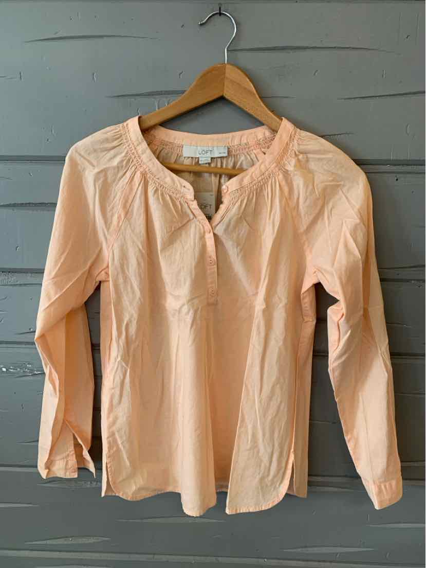 Light peach long-sleeve blouse with round neckline and relaxed fit on wooden hanger against gray background.