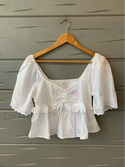 White cropped blouse with eyelet fabric, puffed short sleeves, square neckline, and ruffled hem.