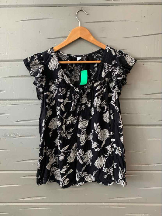 Black floral short-sleeve blouse with ruffle details hanging on wooden hanger.
